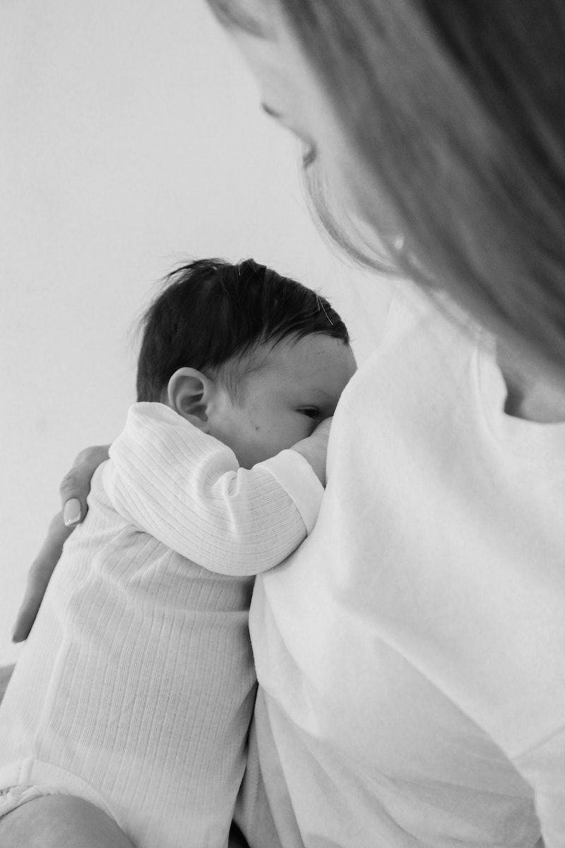 Grayscale Photo of a Mother Carrying Her Baby while Breastfeeding